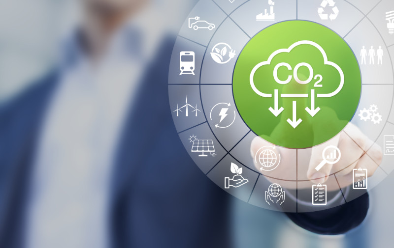 Person pointing at a digital screen displaying a CO2 reduction icon surrounded by various sustainability symbols.